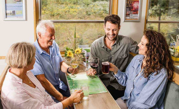 Blick auf vier Erwachsene, die im Zug sitzen und etwas trinken.