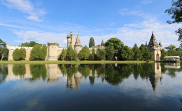 Blick auf einen Teich und im Hintergrund sieht man Bäume und die Mauern und Türme von Schloss Laxenburg.