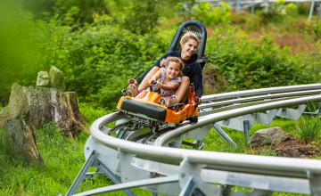 Eine Frau und ein Kind fahren mit einer orangen Sommerrodelbahn in einer Kurve.