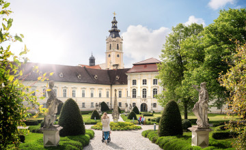 Besucher schlendern durch den grünen Stiftsgarten, immer mit Blick auf das Benediktinerstift Altenburg.