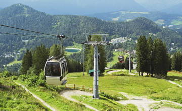 Blick von oben auf eine Kabinenbahn. Im Hintergrund ist der Ausblick ins Tal mit Bäumen und ganz unten einem kleinen Speichersee.