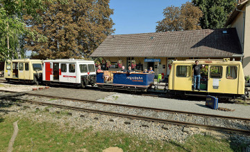 Historischer Bahnhof mit mehreren kleinen, nostalgischen Schienenwagons und Menschen, die die Fahrt genießen.