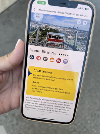 Hand hält Mobiltelefon, Display zeigt NÖ-CARD App mit Riesenrad-Inhalt