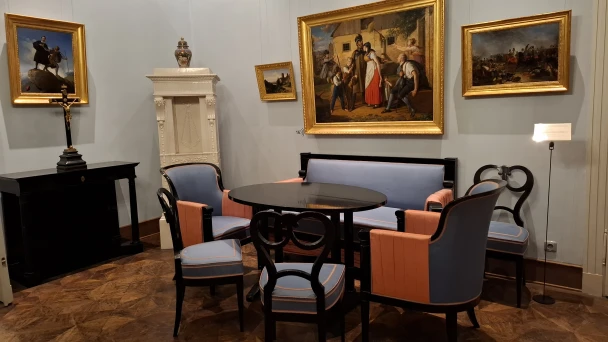 Blick auf Tisch, Stühle und Wandgemälde im Innenraum des Museums.