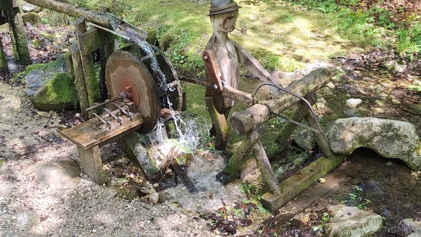 Blick auf den Wasserlauf und ein Wasserrad aus Holz mit geschnitztem Holzfäller.